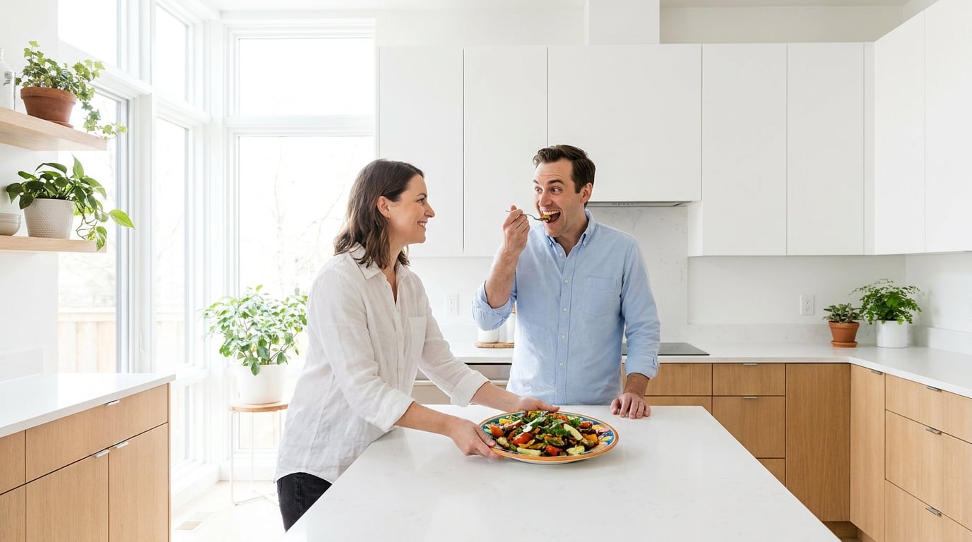 A woman sets down a colourful plate in a bright modern kitchen while her husband takes a bite and lights up
